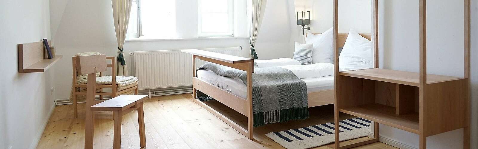 <p>Moderne Schlafzimmermöbel aus hellem Holz stehen in einem lichtdurchfluteten Zimmer. Cremefarbene Vorhänge und der Holzfußboden tragen zur Natürlichkeit bei.</p>