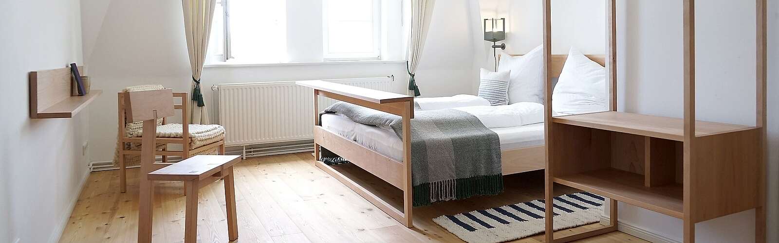 <p>Moderne Schlafzimmermöbel aus hellem Holz stehen in einem lichtdurchfluteten Zimmer. Cremefarbene Vorhänge und der Holzfußboden tragen zur Natürlichkeit bei.</p>