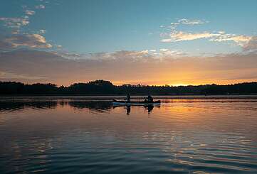 <p>Eine Frau und ein Mann machen eine Kanutour bei Sonnenuntergang auf dem See</p>