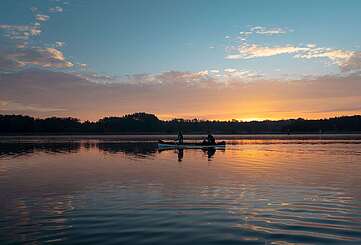 <p>Eine Frau und ein Mann machen eine Kanutour bei Sonnenuntergang auf dem See</p>