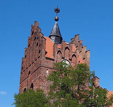<p>Über die dichten, sommerlich grünen Laubbäume hinweg ragen die prächtigen Staffelgiebel der neugotischen Kirche in Linum.</p>