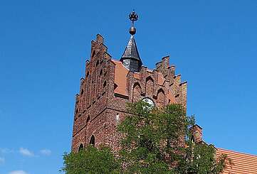 <p>Über die dichten, sommerlich grünen Laubbäume hinweg ragen die prächtigen Staffelgiebel der neugotischen Kirche in Linum.</p>