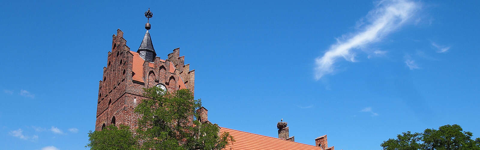 <p>Über die dichten, sommerlich grünen Laubbäume hinweg ragen die prächtigen Staffelgiebel der neugotischen Kirche in Linum.</p>