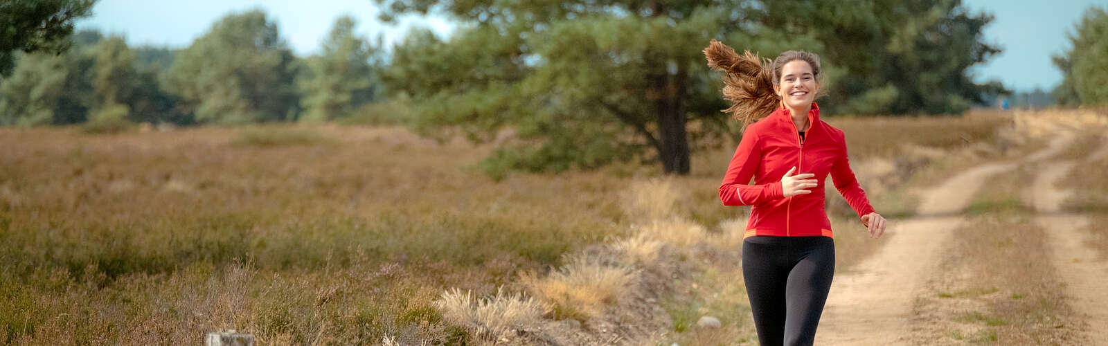 <p>Eine junge Frau joggt auf einem Sandweg durch die Kyritz-Ruppiner Heide</p>