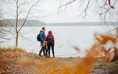 <p>Eine Familie aus Vater, Mutter und Kind steht am herbstlichen Seeufer.</p>