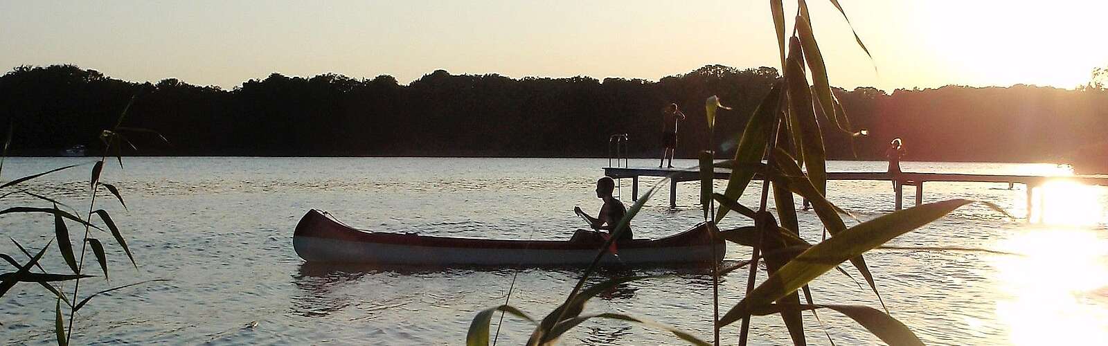 <p>Eine Person fährt in der Abenddämmerung Kanu. Die untergehende Sonne spiegelt sich im Wasser.</p>