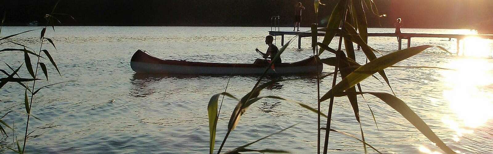 <p>Eine Person fährt in der Abenddämmerung Kanu. Die untergehende Sonne spiegelt sich im Wasser.</p>