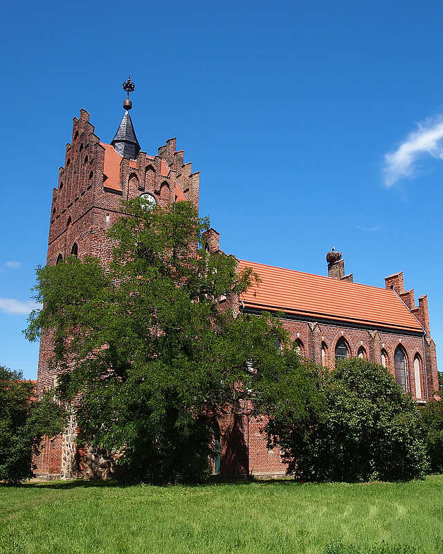 <p>Über die dichten, sommerlich grünen Laubbäume hinweg ragen die prächtigen Staffelgiebel der neugotischen Kirche in Linum.</p>