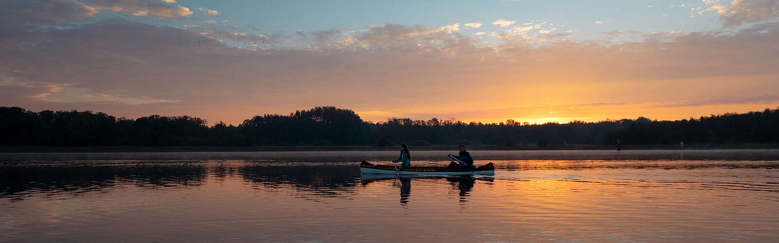<p>Eine Frau und ein Mann machen eine Kanutour bei Sonnenuntergang auf dem See</p>