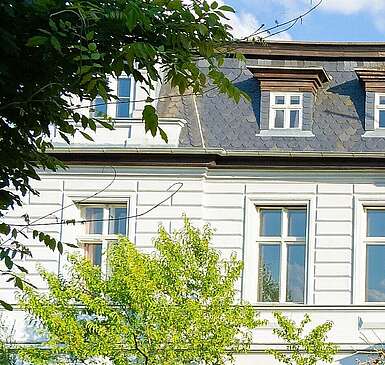 <p>Ein Treppe führt zur roten Eingangstür des weißen eindrucksvollen Hotels auf dem Gut Boltenhof. Die Hecken und und der Rasen um das Gebäude leuchten in der Sonne.</p>