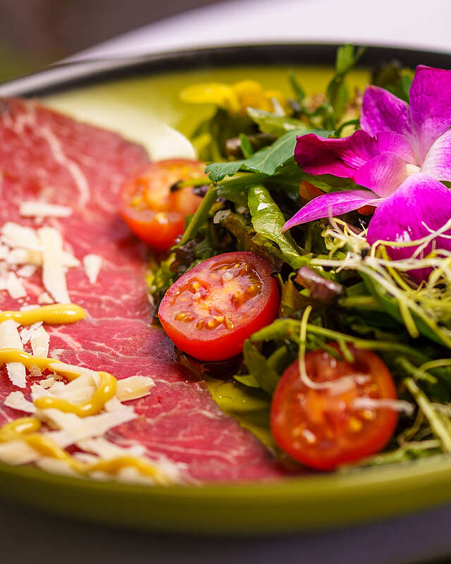 <p>Fotos eines grünen, hübsch angerichteten Tellers mit roter Salami, kleinen Tomatenhälften, Salat und violetten Blüten.</p>