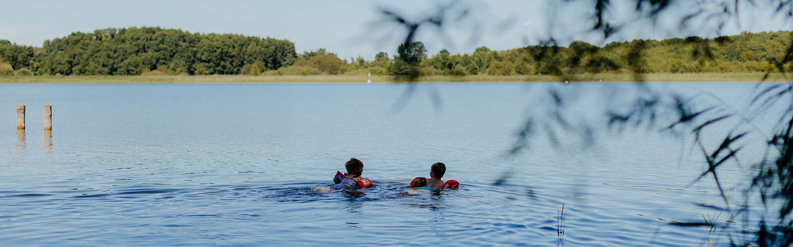 <p>Zwei kleine Kinder mit Schwimmflügeln schwimmen bei Sommerwetter im See.</p>