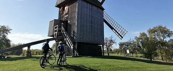 <p>Zwei Radfahrer blicken auf die Bockwindmühle Vehlefanz</p>